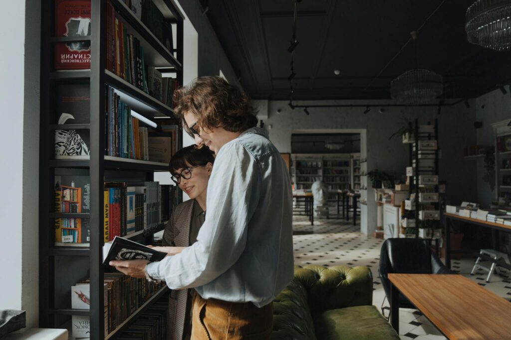 Two adults browsing books in a stylish library, sharing joy and knowledge.